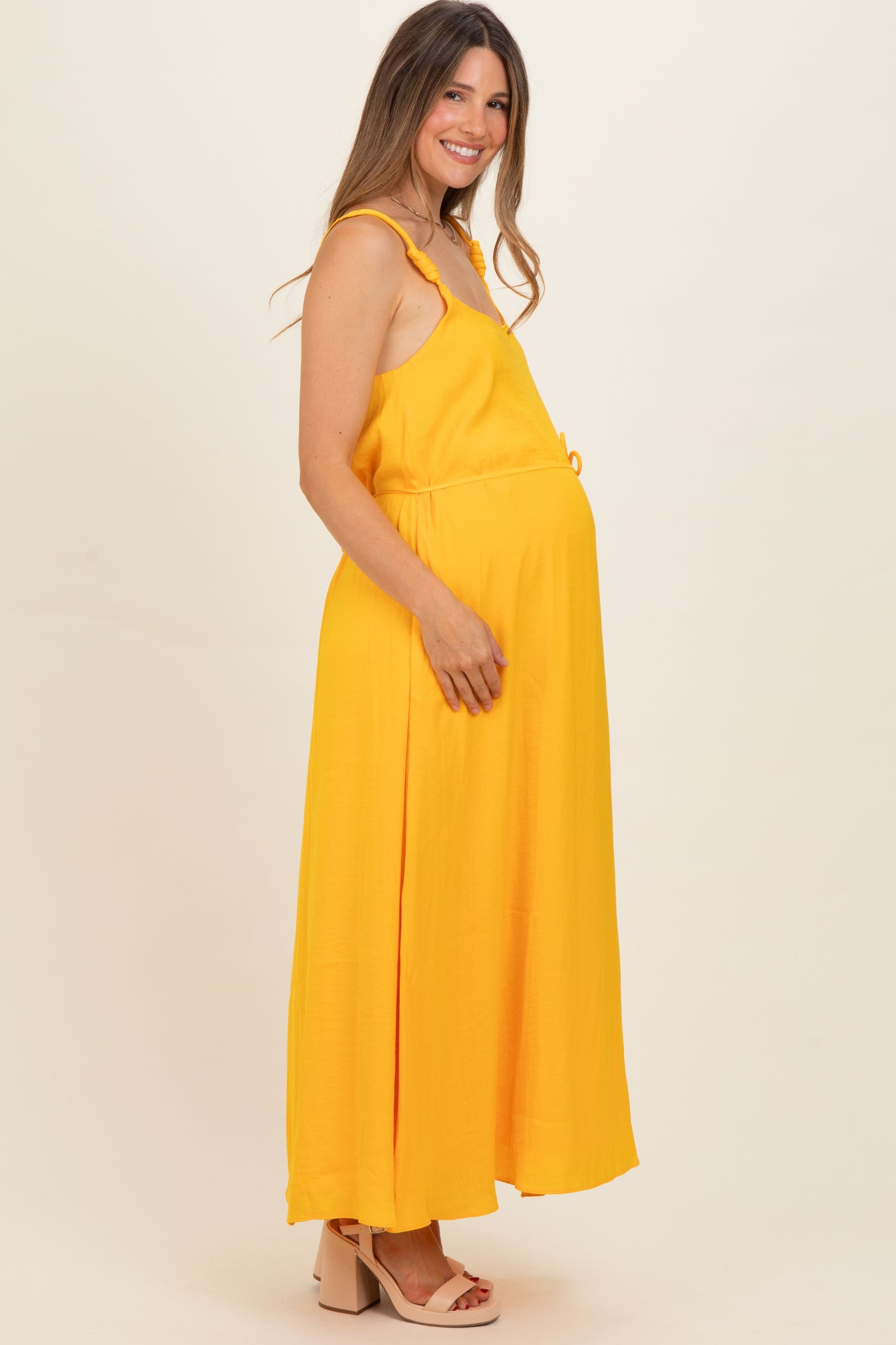 woman wearing a yellow sleeveless maternity maxi dress with a drawstring waist and visible baby bump