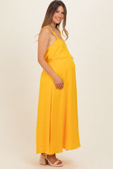 woman wearing a yellow sleeveless maternity maxi dress with a drawstring waist and visible baby bump
