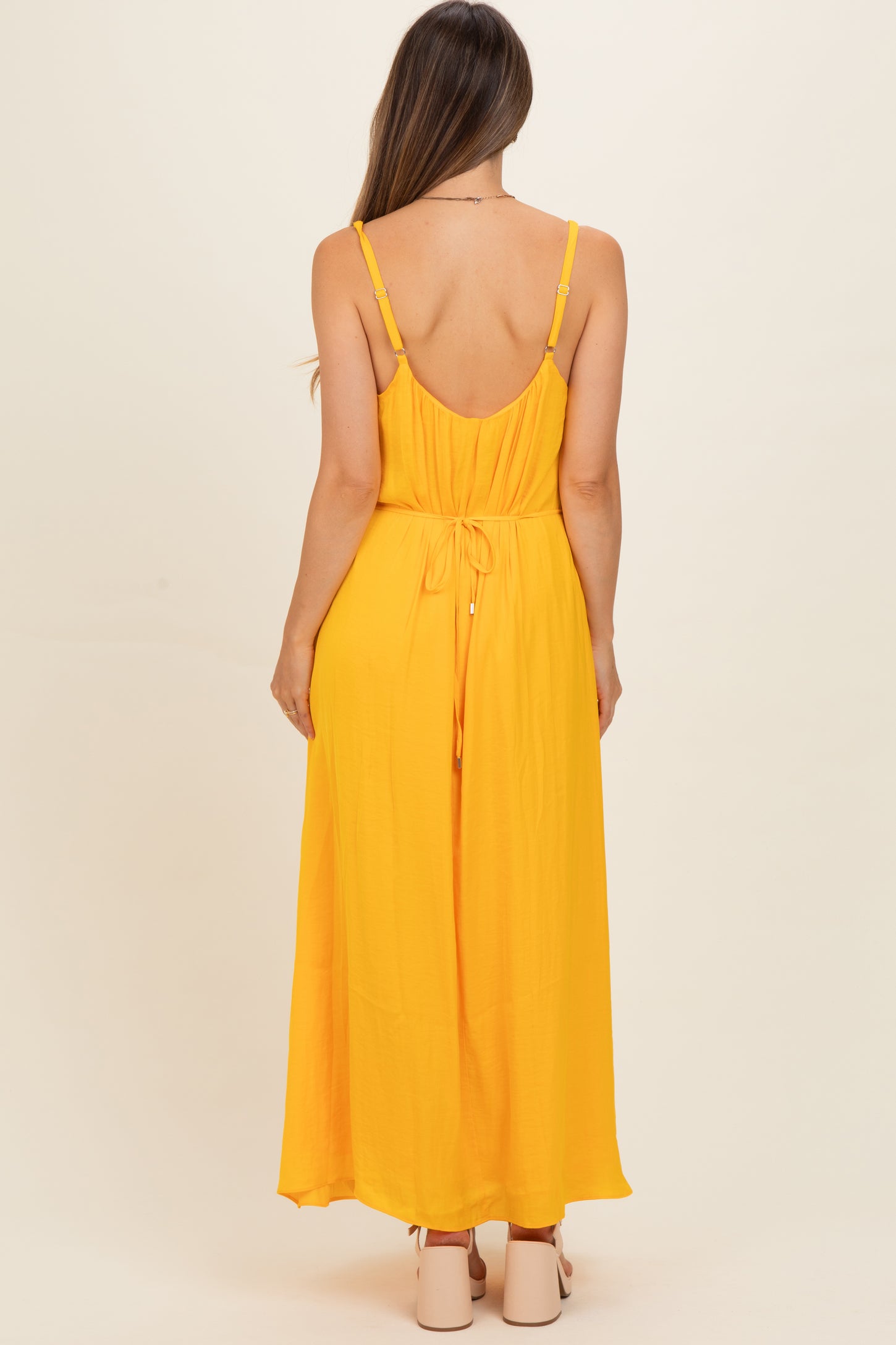 woman wearing a bright yellow maternity maxi dress with adjustable straps and a tied back detail