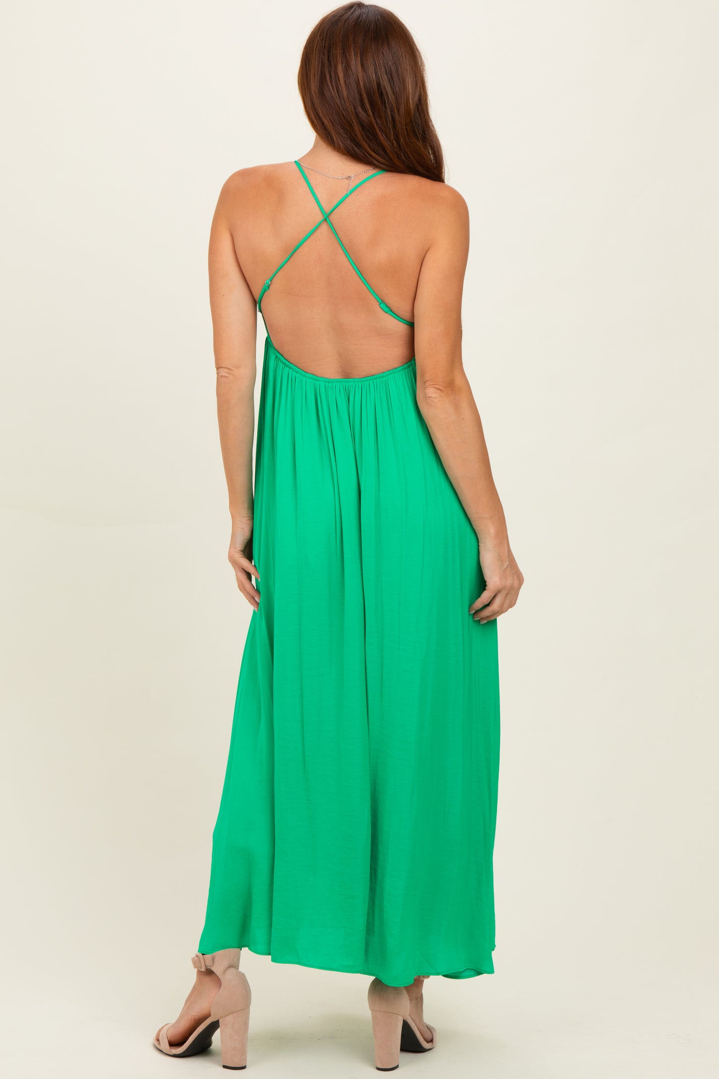 woman wearing a green backless maxi dress with cross-strap detailing and a flowing silhouette