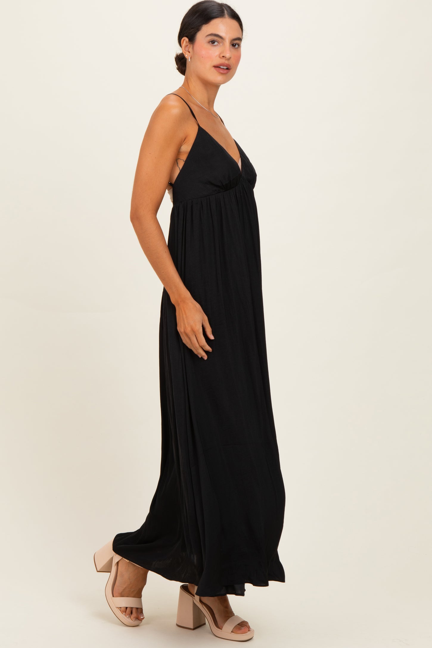 woman wearing a black maxi dress with spaghetti straps and a flowing silhouette standing in profile