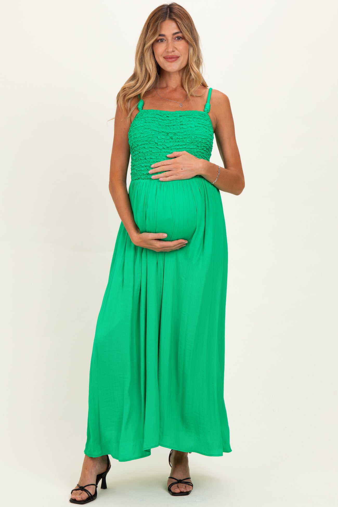 woman wearing a bright green maternity maxi dress with a ruched bodice and holding her baby bump