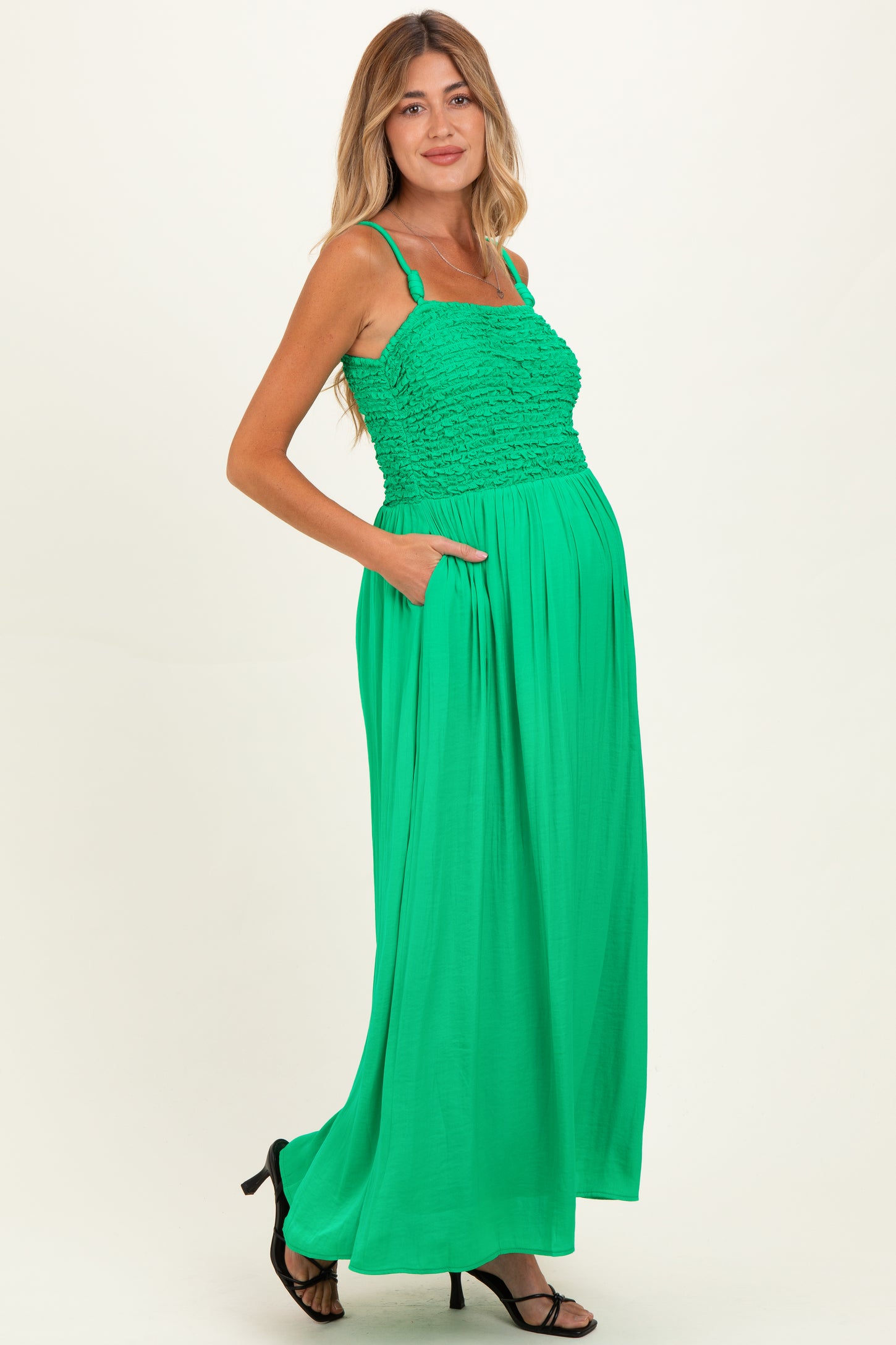 woman wearing a bright green maternity maxi dress with a smocked bodice and pockets, showing her baby bump
