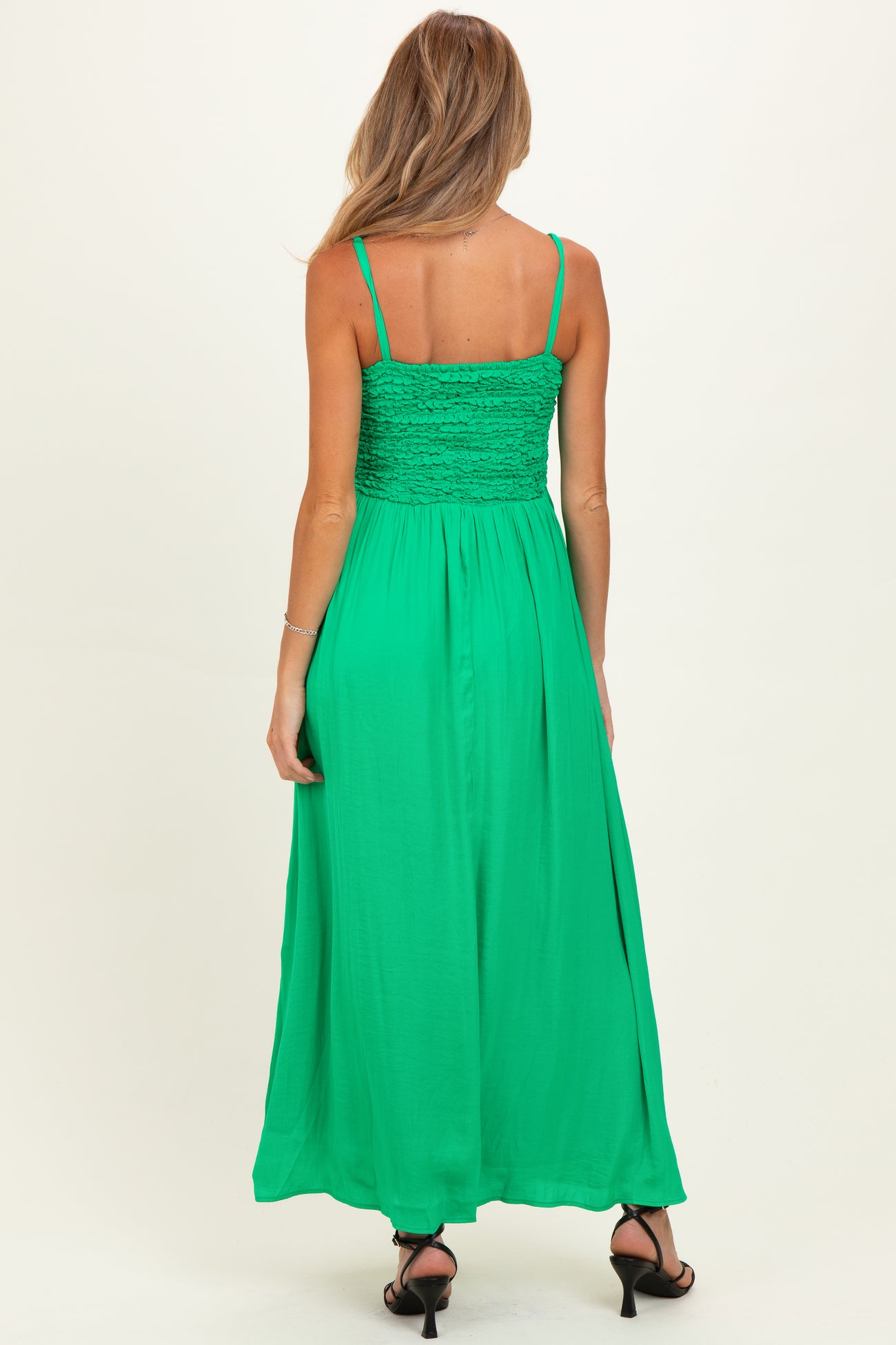 woman wearing a green maternity maxi dress with smocked bodice and spaghetti straps, showing a baby bump from the back