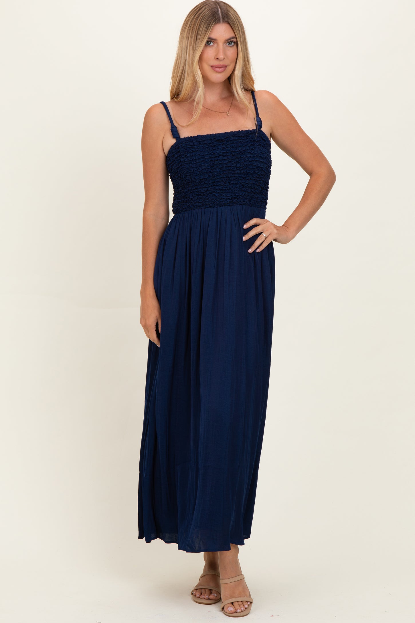 woman wearing a navy blue maxi dress with a smocked bodice and thin straps, standing on a neutral background