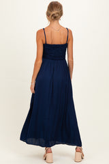 woman wearing a navy blue maternity maxi dress with a smocked bodice and adjustable straps, showing the back view