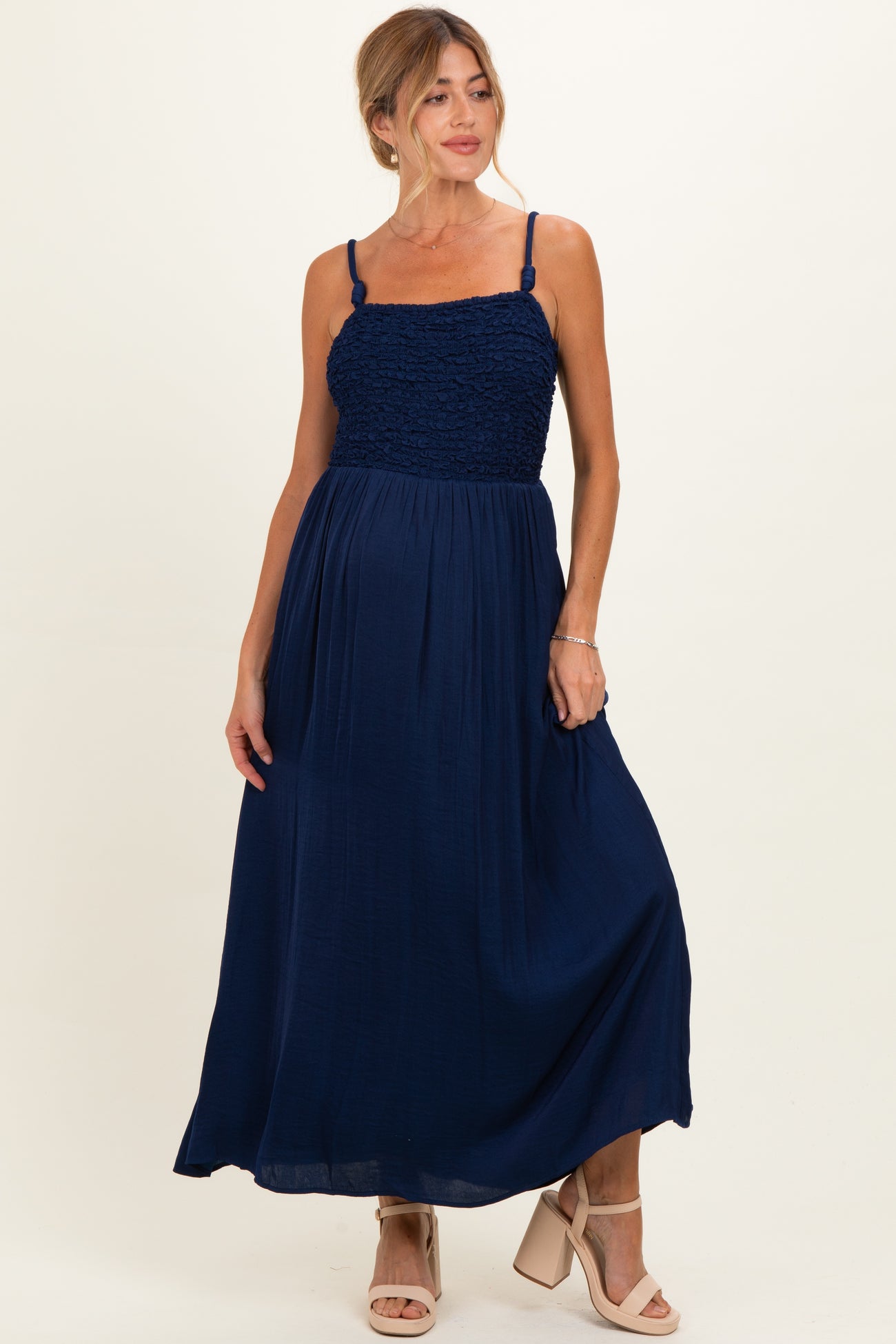 woman wearing a navy blue maternity maxi dress with smocked bodice and spaghetti straps, showcasing her baby bump