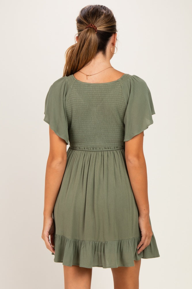 woman wearing a sage green maternity dress with flutter sleeves and a ruffled hem, back view