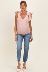 woman wearing a pink maternity top with tie straps and a visible baby bump, paired with blue jeans