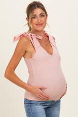 woman wearing a light pink maternity top with bow tie straps and showing her baby bump