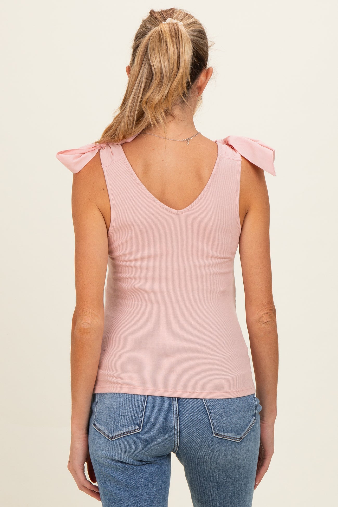 woman wearing a light pink ribbed maternity tank top with bow tie shoulder details, back view