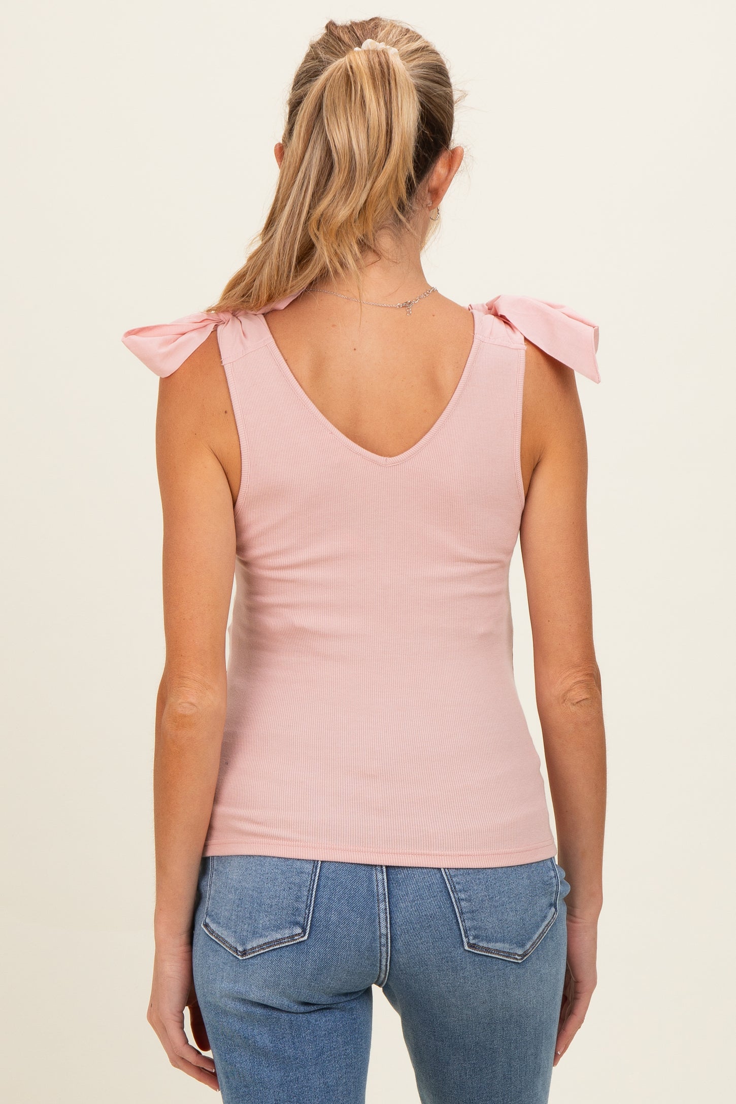 woman wearing a light pink ribbed maternity tank top with bow tie shoulder details, back view