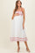 woman wearing a white maternity dress with red floral embroidery and holding her baby bump