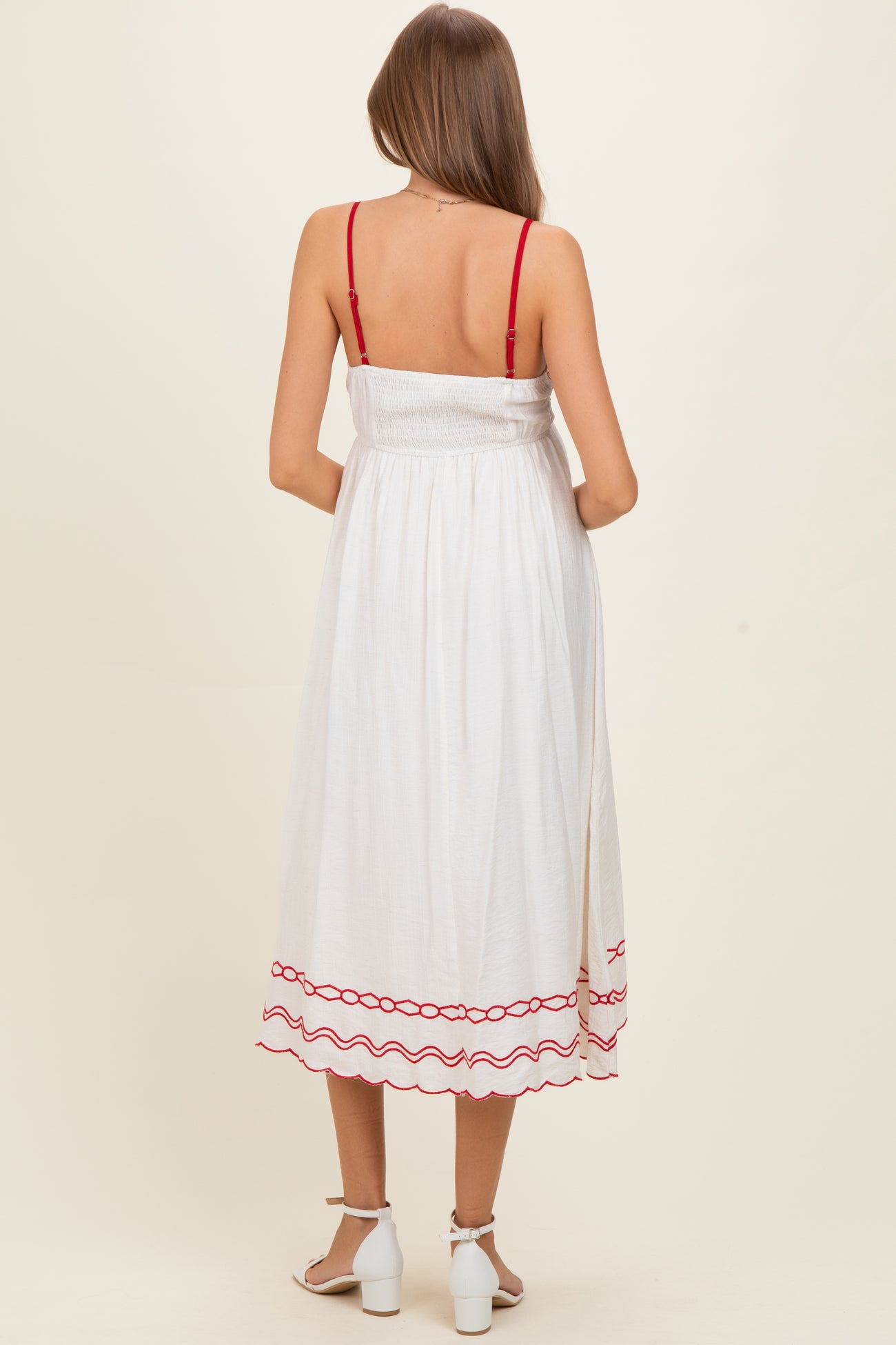 woman wearing a white maternity dress with red trim and adjustable straps, showing a baby bump from the back