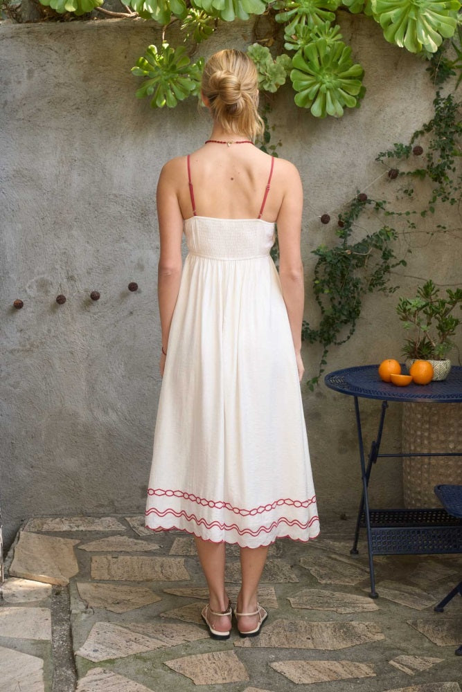 woman wearing a white midi sundress with red detailing and adjustable straps, showing the back view in a garden setting