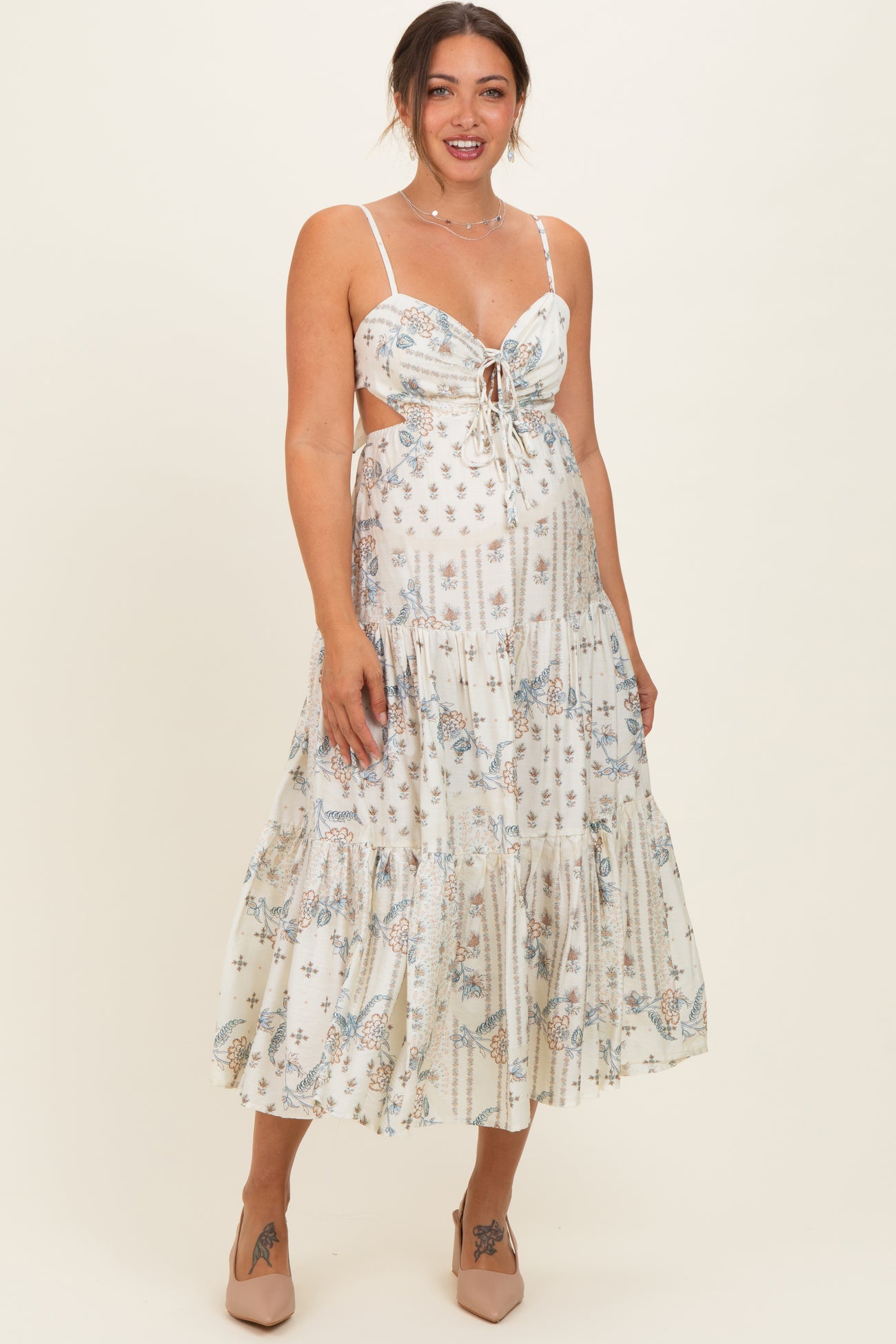 woman wearing a white floral print maternity maxi dress with a tied front and spaghetti straps, smiling at the camera