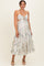 woman wearing a white floral print maternity maxi dress with a tied front and spaghetti straps, smiling at the camera