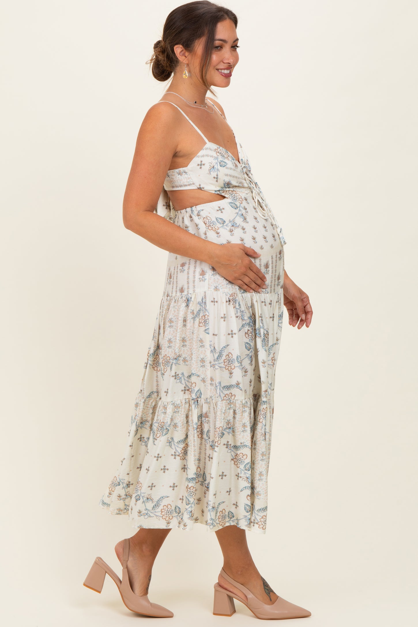 woman wearing a cream floral maternity maxi dress, showing her baby bump with a side profile pose