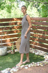 woman wearing a striped sleeveless midi dress with a side slit, standing outdoors with greenery in the background