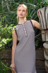 woman wearing a striped sleeveless dress with button detailing, posed outdoors among greenery