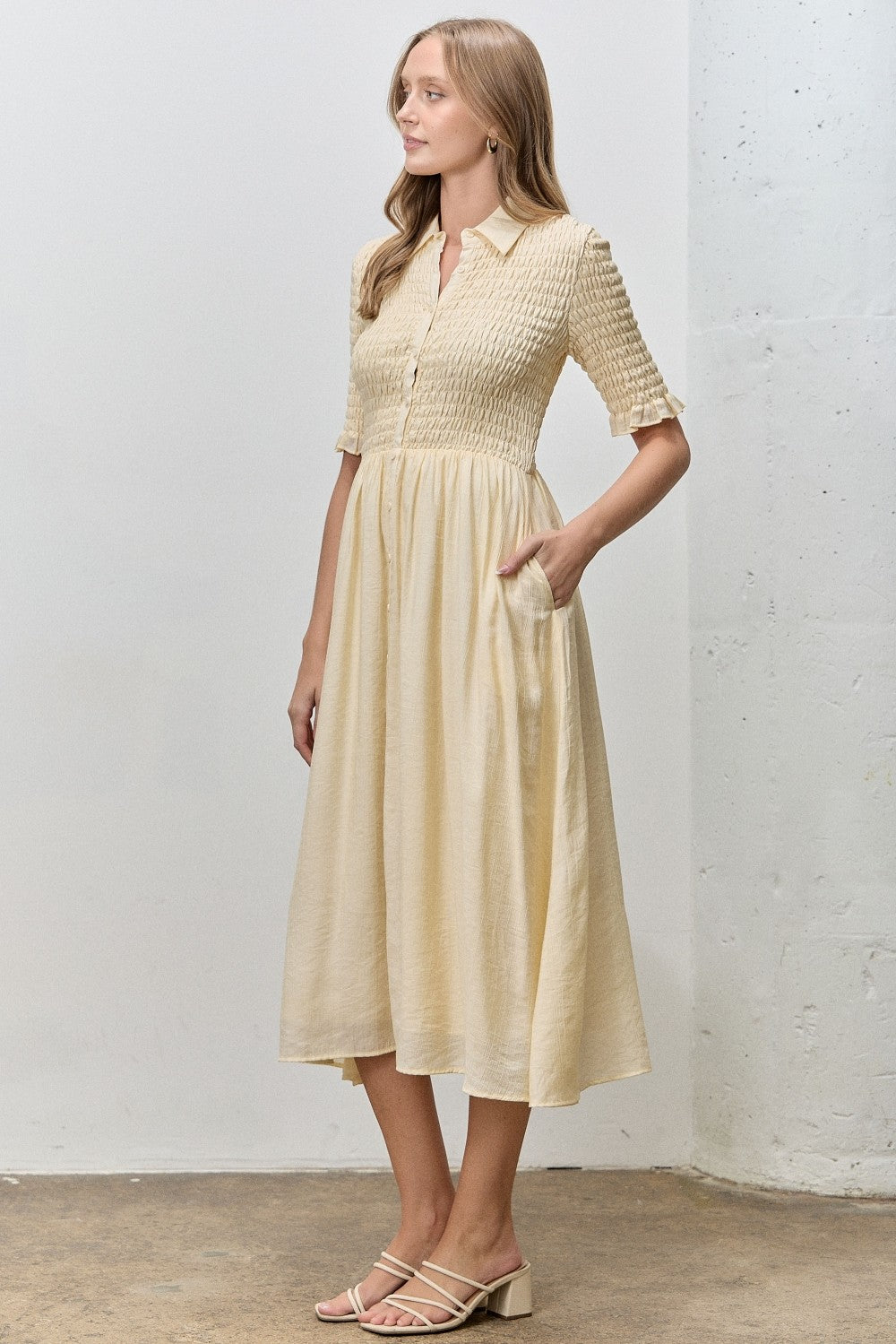 woman wearing a cream short sleeve button-up dress with a smocked bodice and pockets, standing against a neutral background