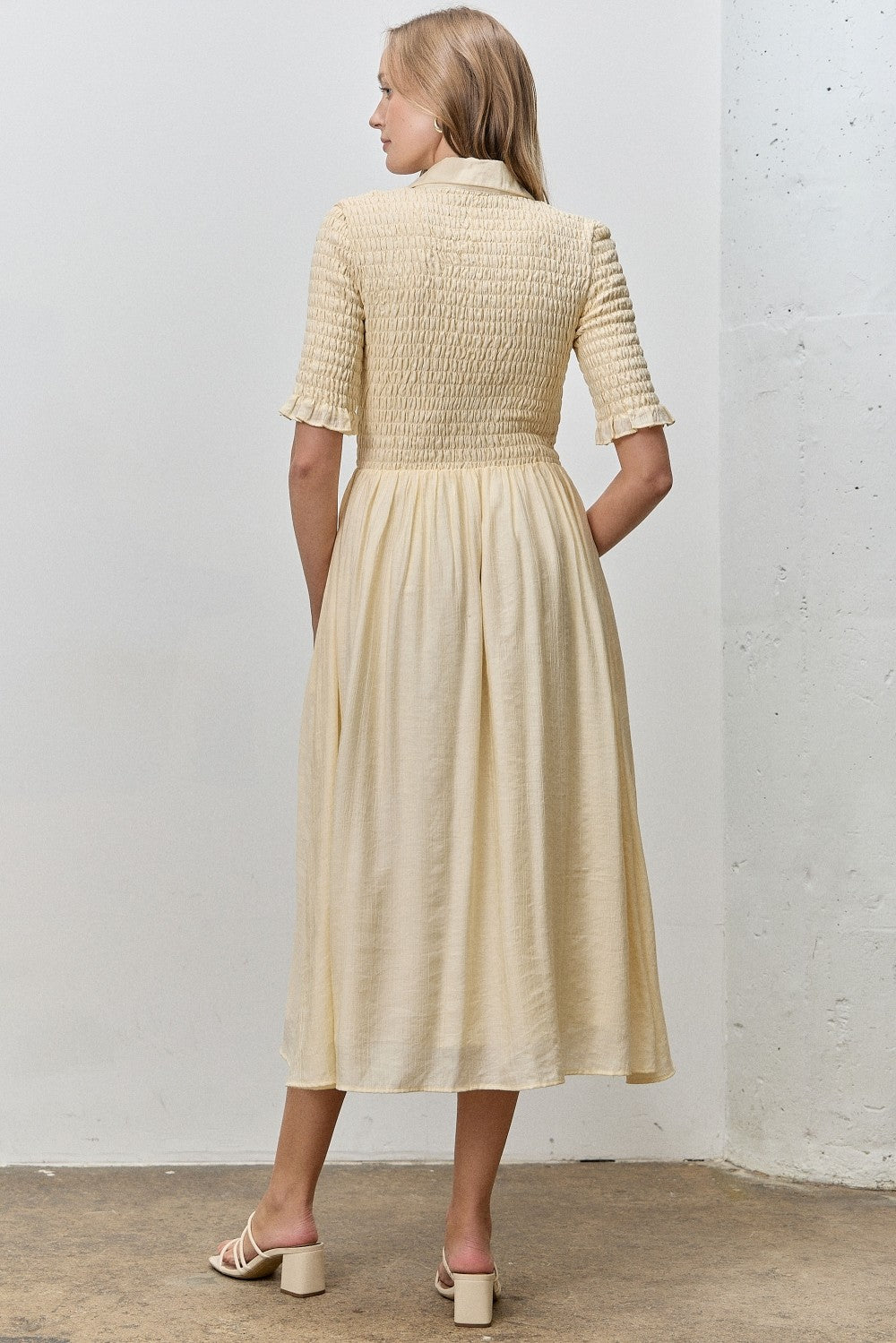 woman wearing a cream-colored smocked midi dress with short sleeves, shown from the back