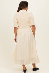 woman wearing a cream-colored maternity dress with a smocked bodice and ruffled sleeves, showing a relaxed fit