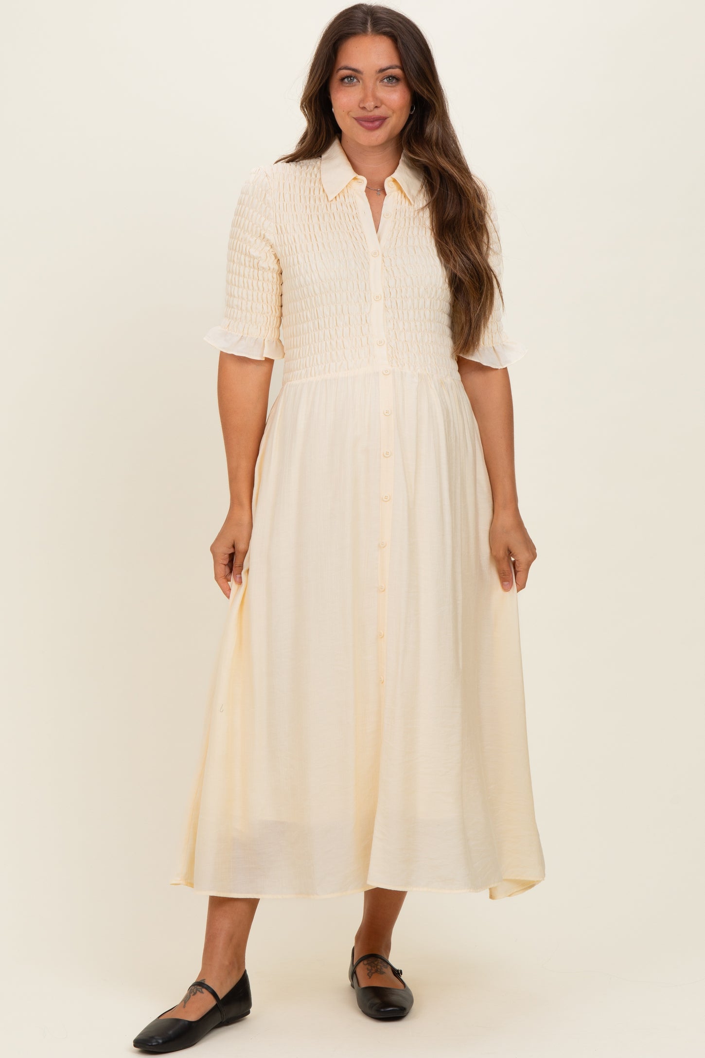 woman wearing a cream maternity dress with a smocked bodice, short sleeves, and button-down front, styled for comfort