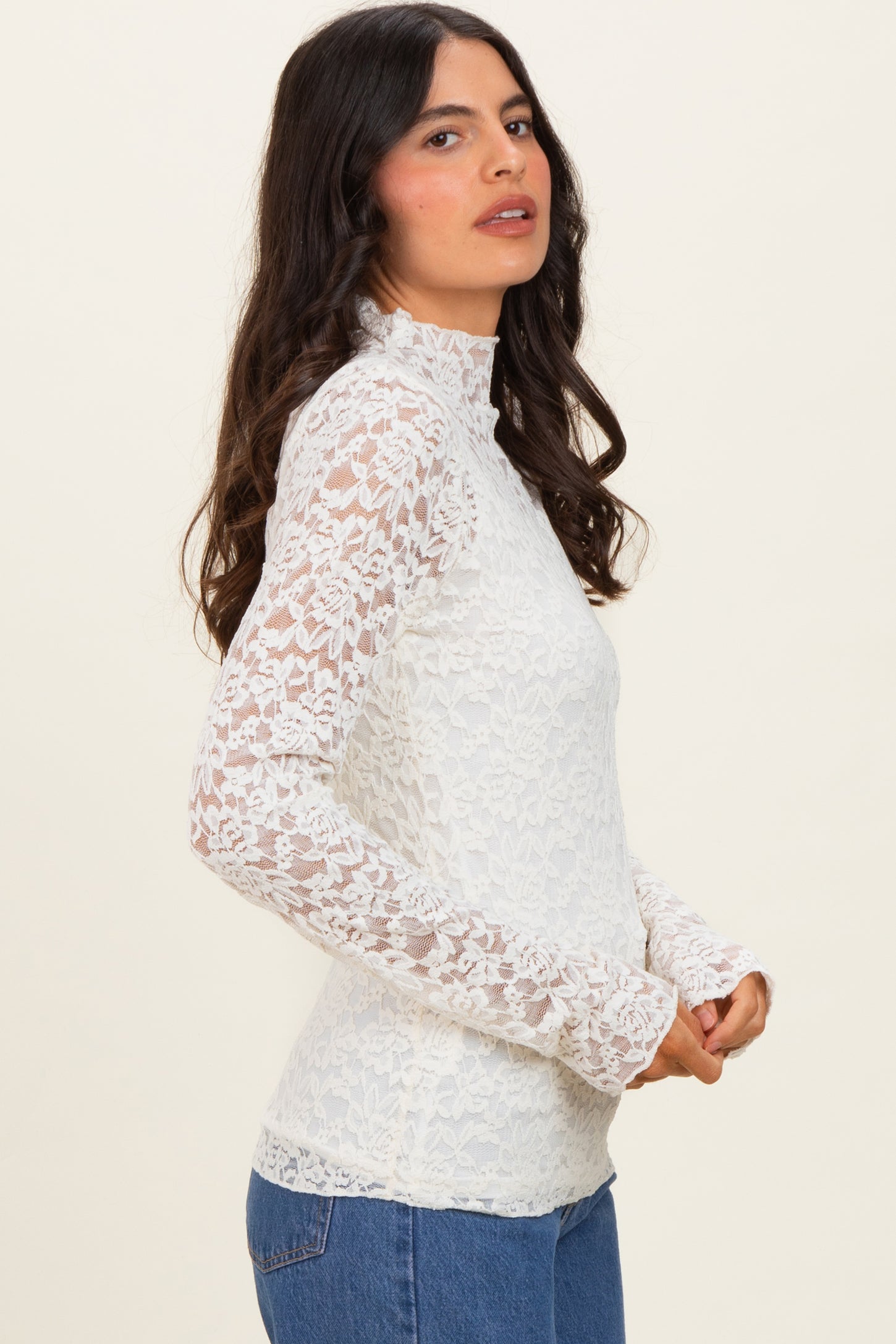 woman wearing a white lace long sleeve top with a high neck and fitted silhouette, paired with blue jeans