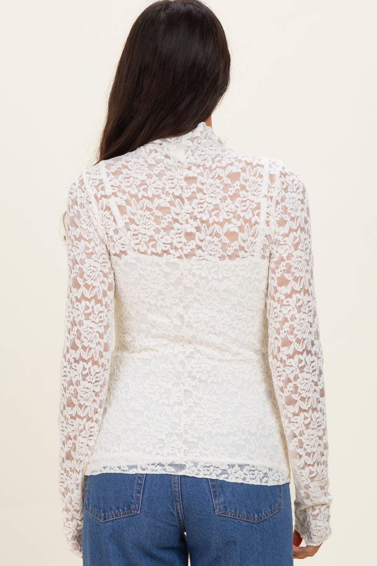 woman wearing a white lace long sleeve top, featuring a sheer back design, paired with blue jeans