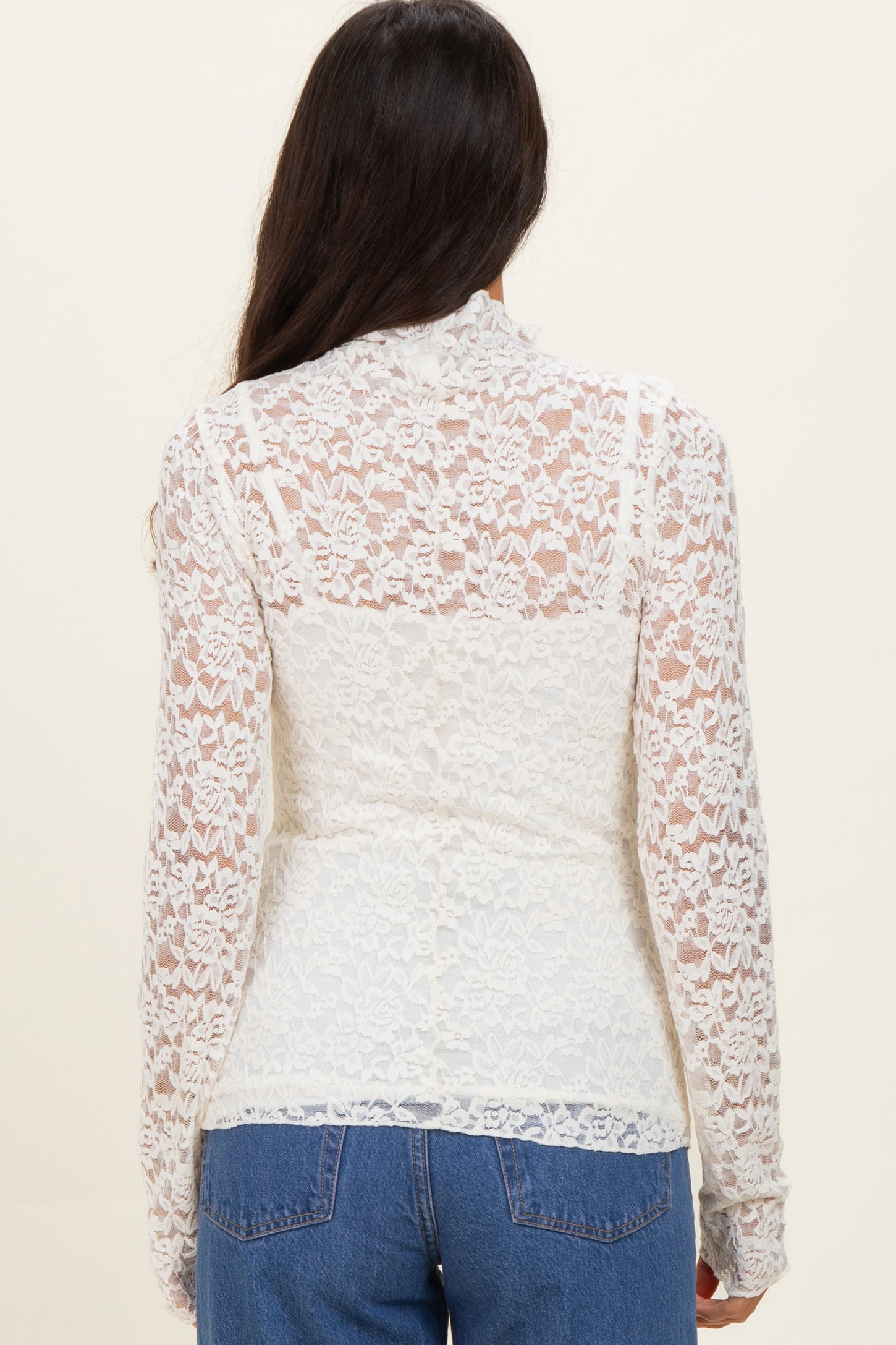woman wearing a white lace long sleeve top, featuring a sheer back design, paired with blue jeans