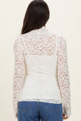 woman wearing a white lace long sleeve top, featuring a sheer back design, paired with blue jeans