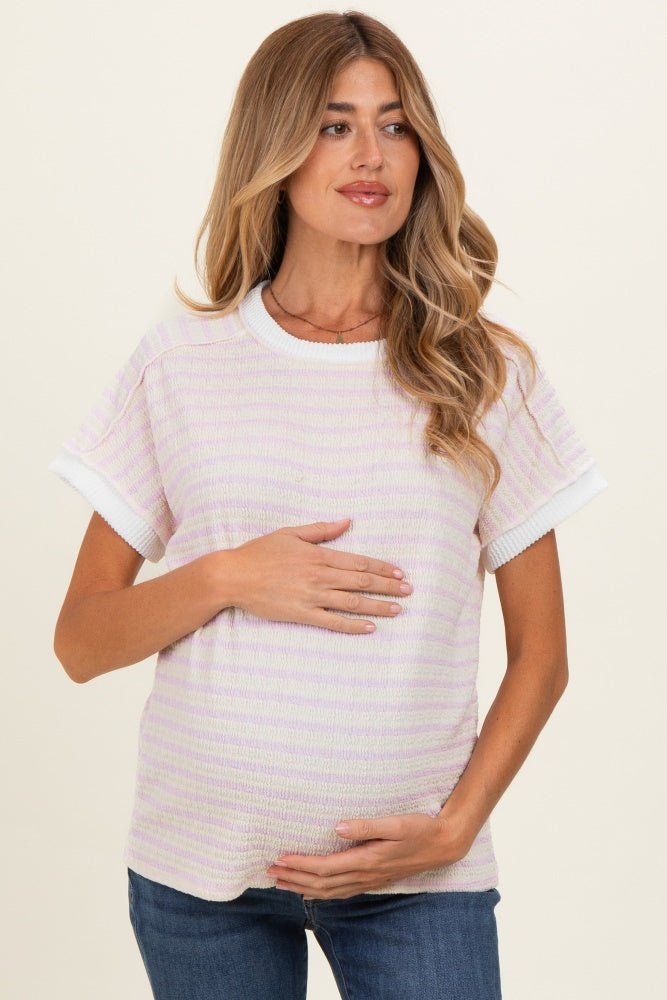 woman wearing a light purple striped maternity top with white trim and holding her baby bump