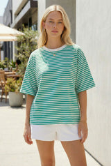 woman wearing a green and white striped oversized t-shirt with short sleeves and white shorts