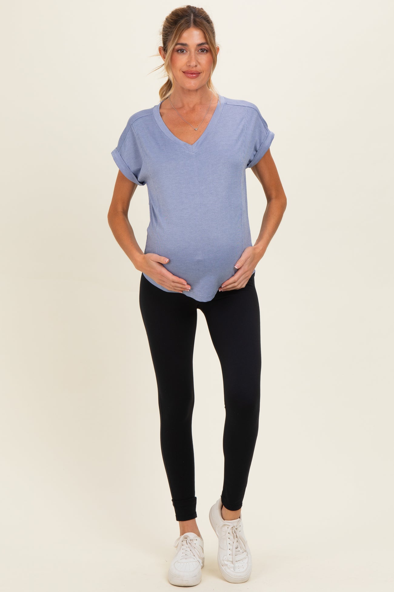 woman wearing a light blue v-neck maternity top and black leggings, showing a visible baby bump