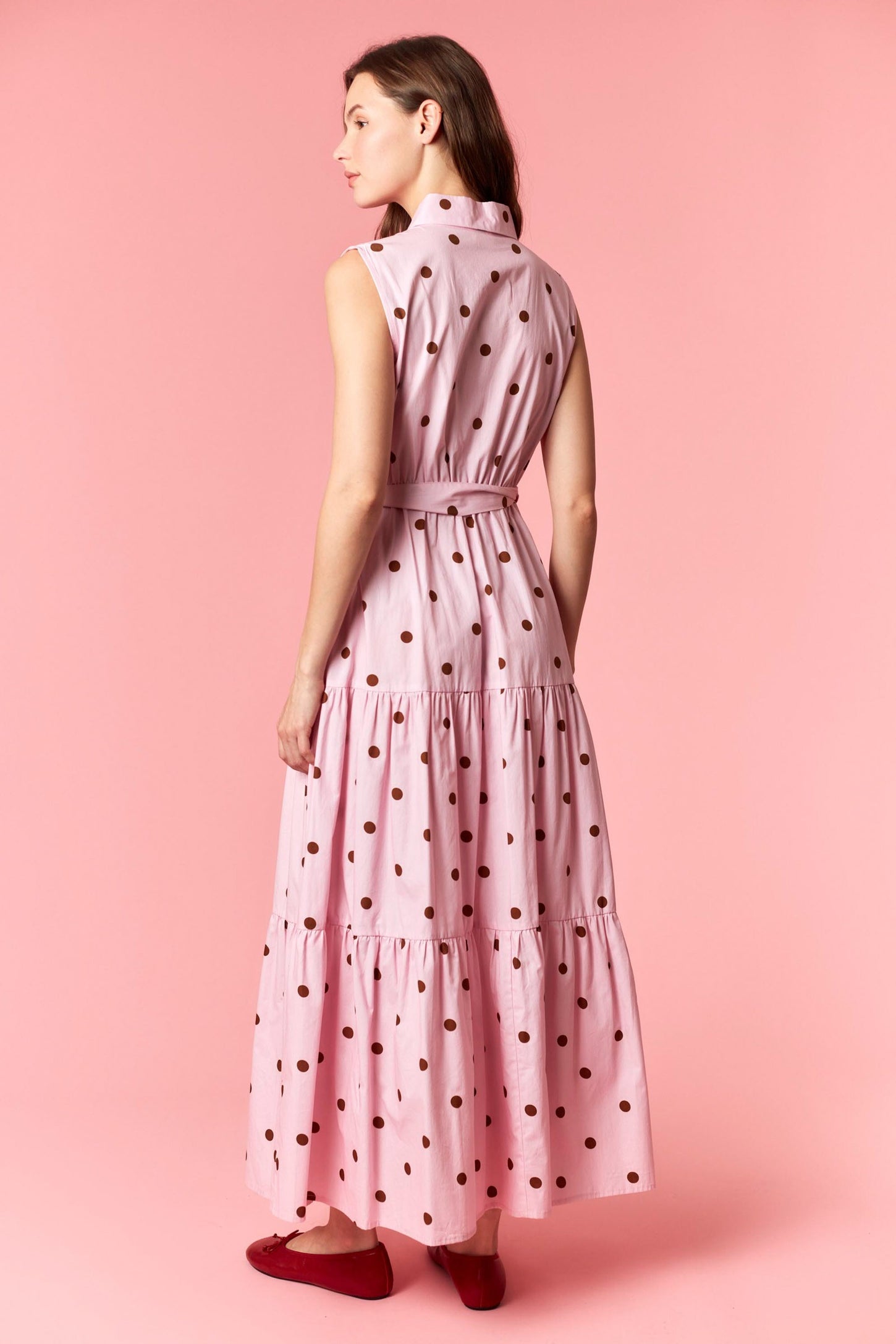 woman wearing a pink polka dot maxi dress with a tiered design and sleeveless style, standing against a pink background