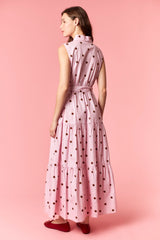 woman wearing a pink polka dot maxi dress with a tiered design and sleeveless style, standing against a pink background