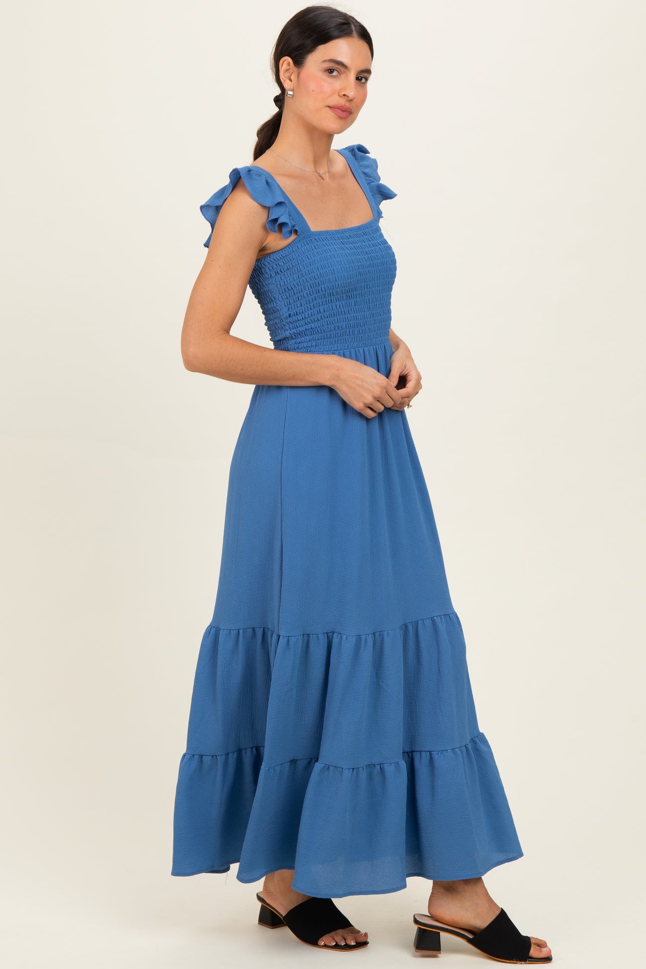 woman wearing a blue maxi dress with ruffled straps and a smocked bodice, standing against a neutral background