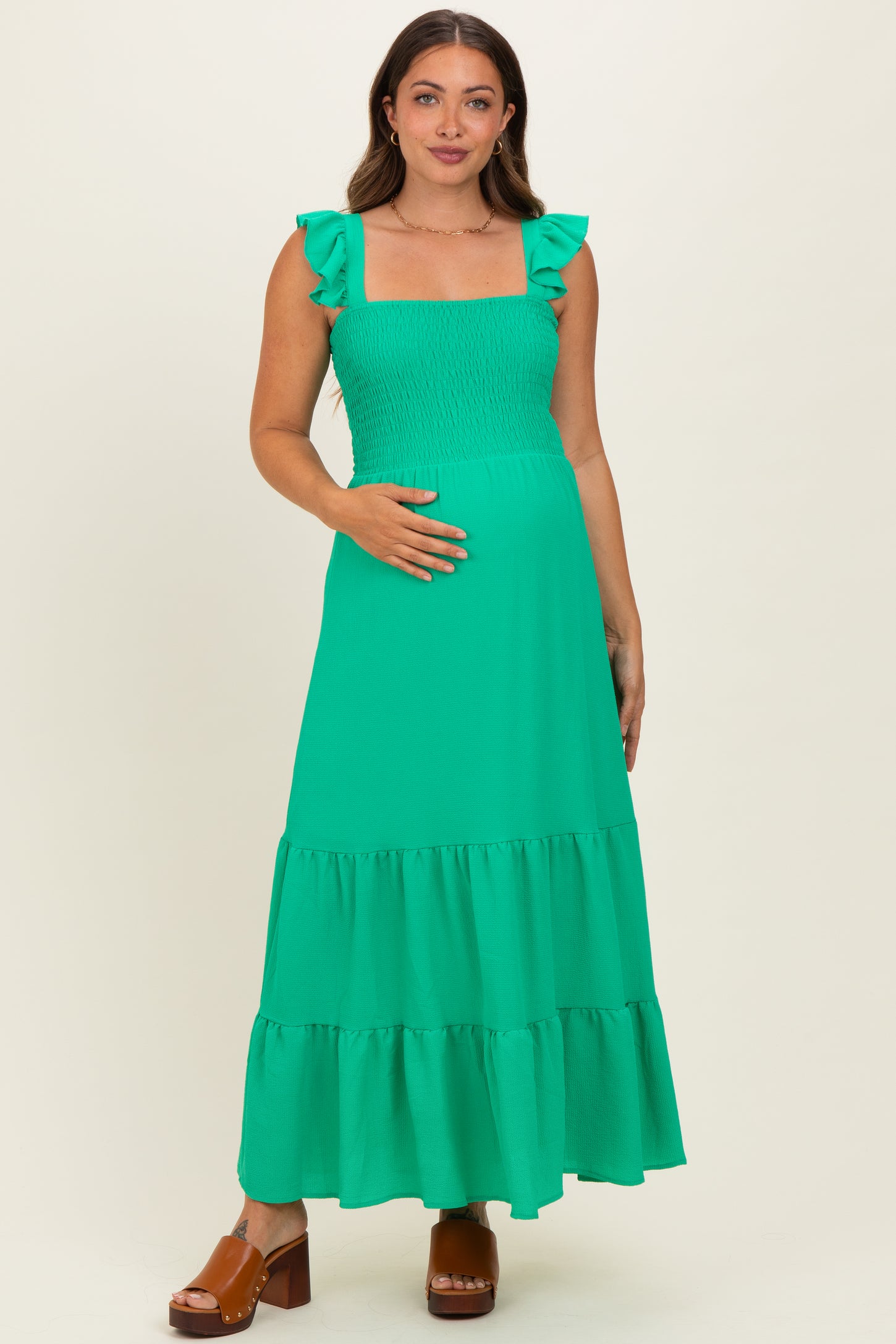 woman wearing a bright green maternity maxi dress with ruffle sleeves and a smocked bodice, showing her baby bump
