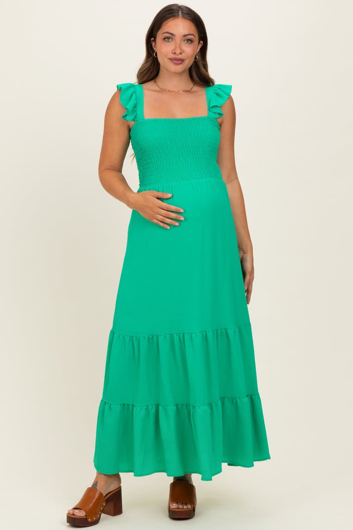woman wearing a bright green maternity maxi dress with ruffle sleeves and a smocked bodice, showing her baby bump