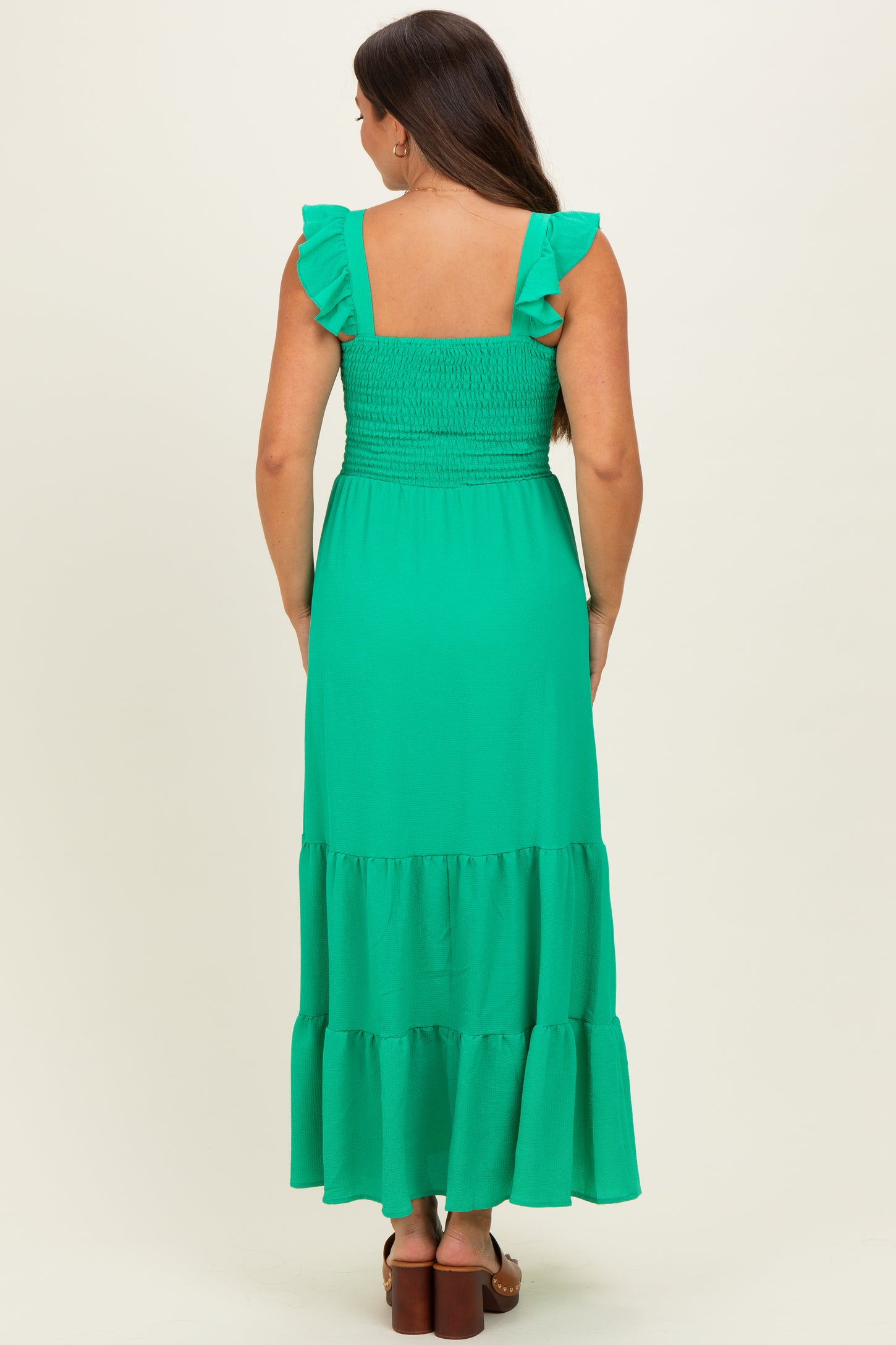 woman wearing a green maternity maxi dress with ruffle straps and a smocked bodice, showing a baby bump from behind