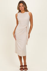 woman wearing a beige sleeveless midi dress with a side knot detail and a fitted silhouette, posing elegantly