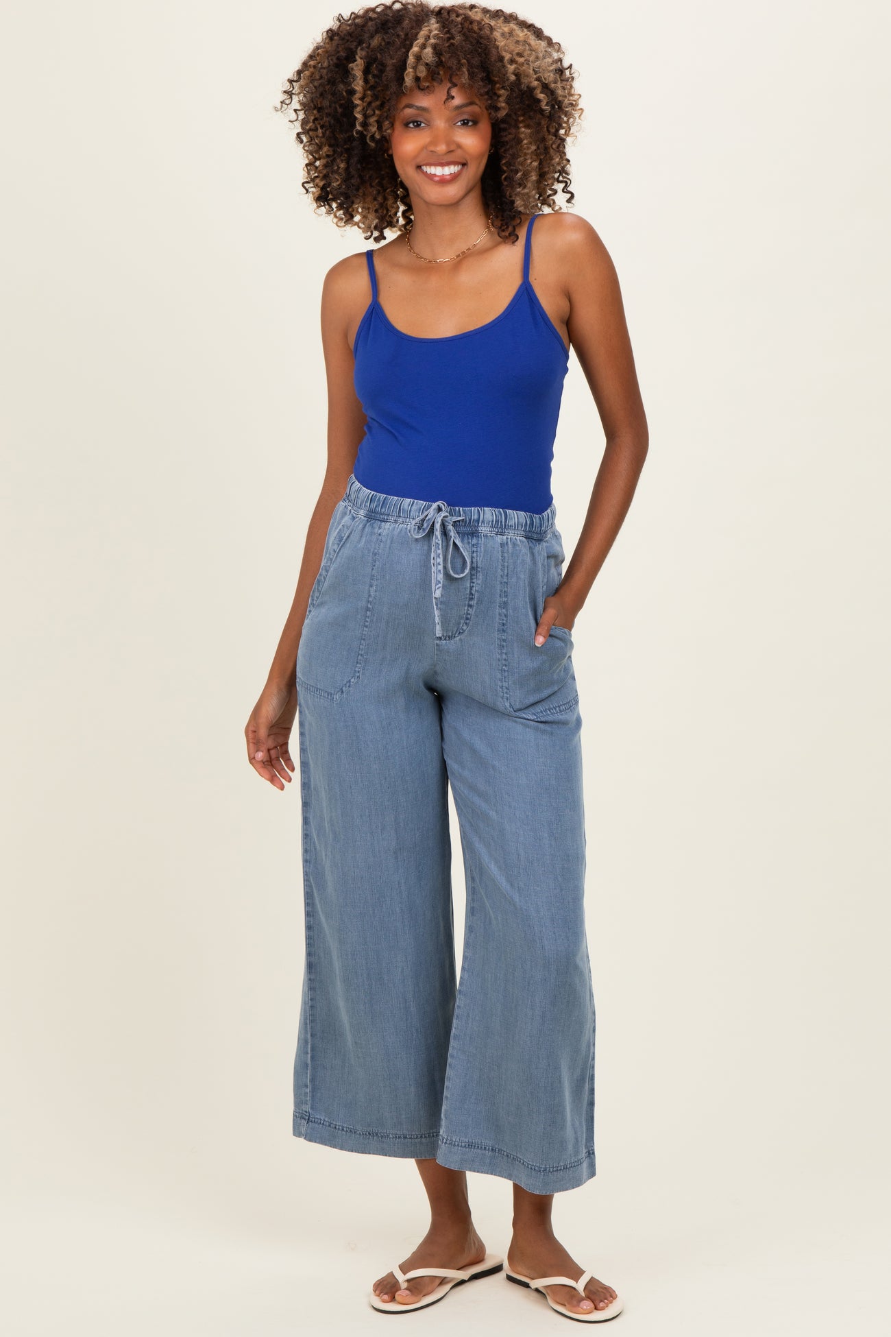 woman wearing a blue maternity tank top and light blue wide-leg maternity pants with pockets and drawstring waistband