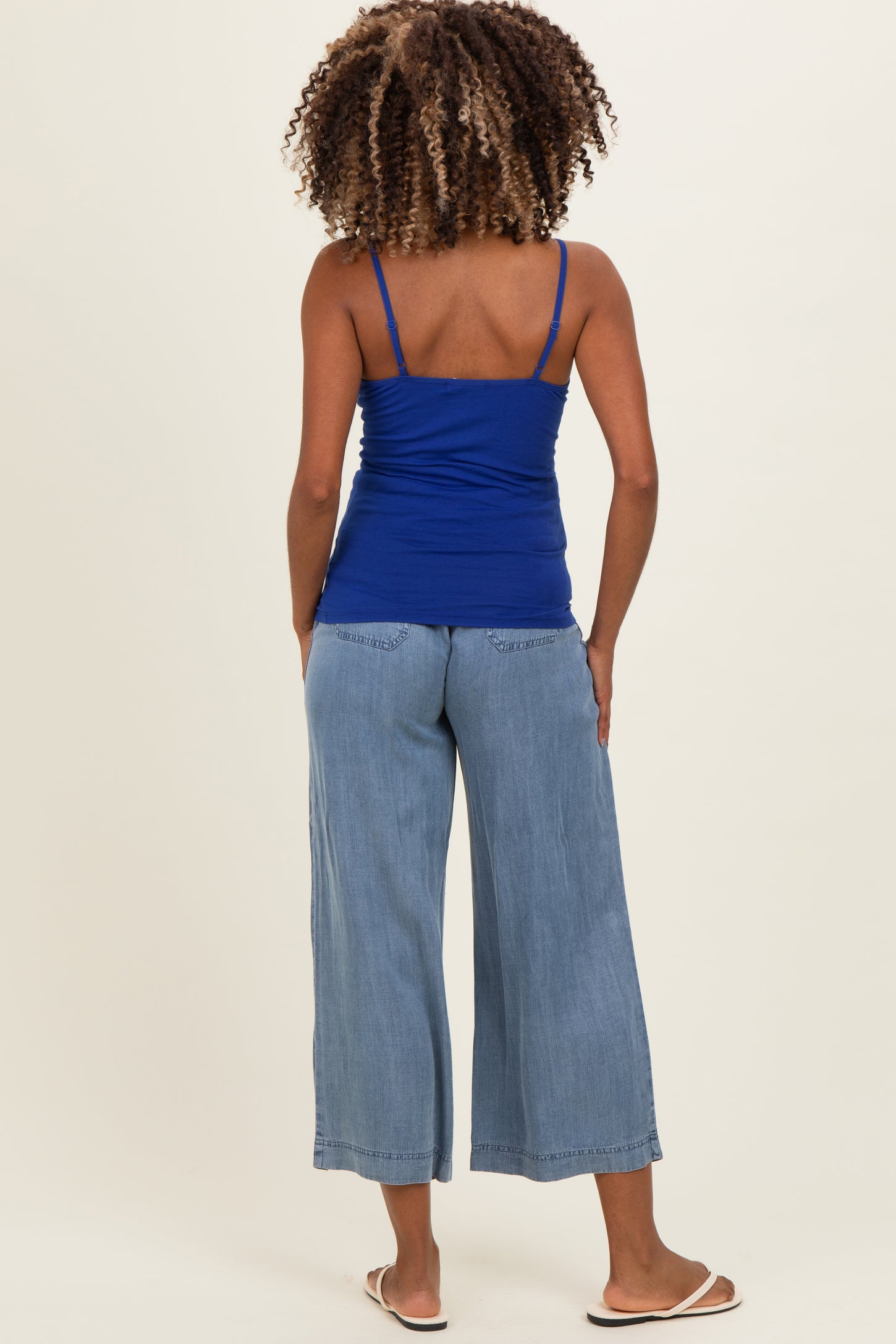 woman wearing a blue maternity tank top and light blue wide-leg jeans, seen from the back
