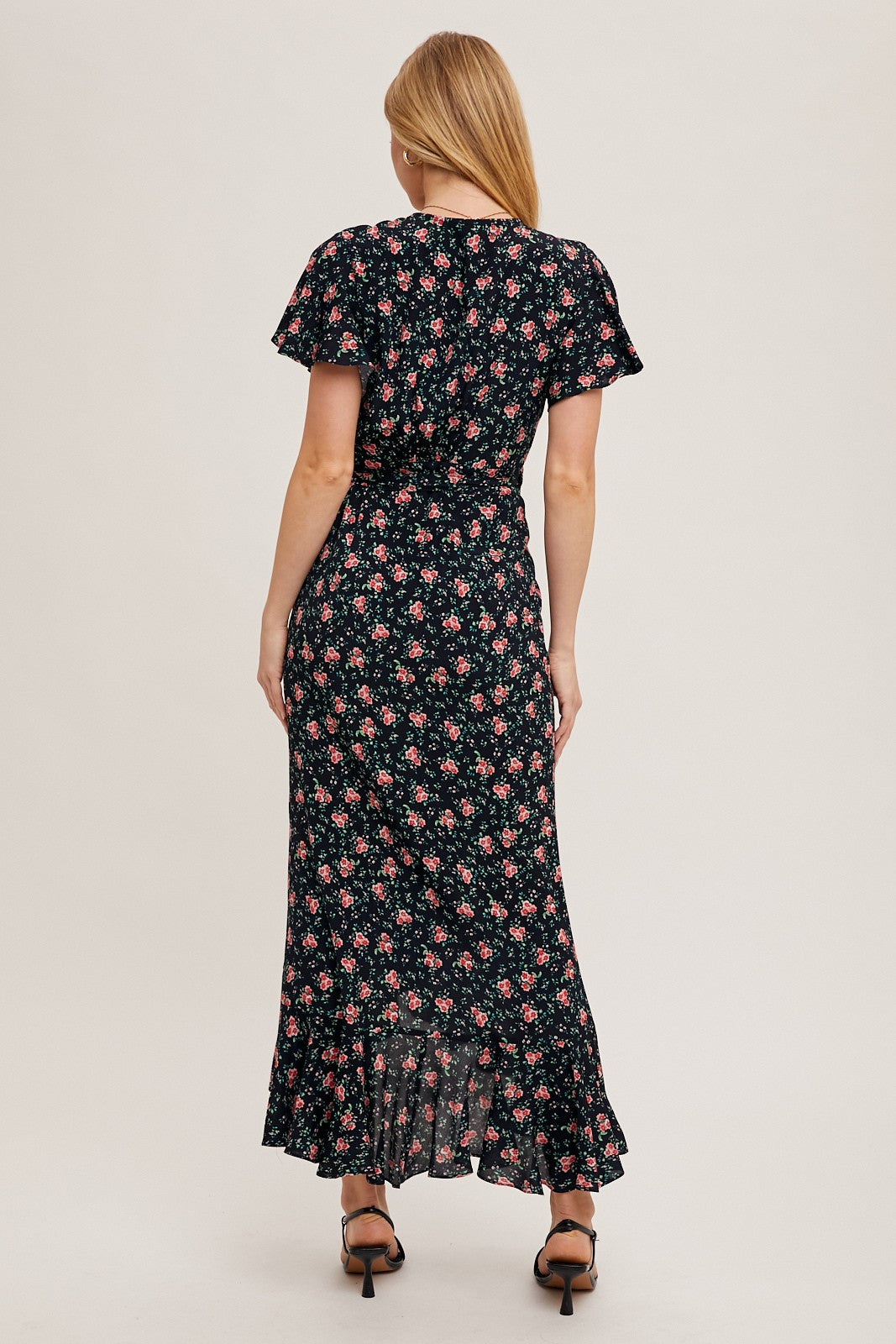 woman wearing a black floral maxi dress with short flutter sleeves and a ruffled hem