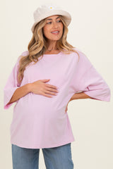 woman wearing a light pink maternity oversized top and holding her baby bump