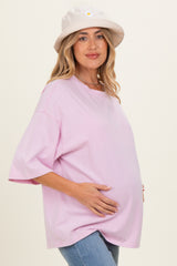 woman wearing a light pink oversized maternity t-shirt and holding her baby bump, styled with a cream bucket hat