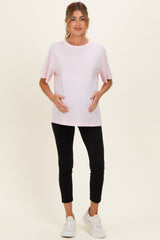 woman wearing a pink short sleeve maternity top and black leggings, holding her baby bump