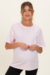woman wearing a light pink short sleeve maternity top and holding her baby bump