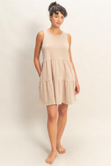 woman wearing a beige sleeveless tiered mini dress standing barefoot
